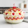 A close-up, direct-angle shot of a vibrant Classic Banana Split Fluff Salad in a clear glass bowl, garnished with pecans and maraschino cherries, showcasing its creamy texture and fresh fruit