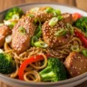 Macro close-up of sticky garlic chicken noodles in a bowl, garnished with green onions and sesame seeds.