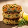 Macro close-up of two golden-brown crispy quinoa and sweet potato patties, one slightly cut to show the tender orange interior, garnished with fresh dill and a lemon wedge on a rustic wooden board.