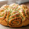 Close-up of golden-brown cheesy garlic herb swirl bread with melted cheese and fresh herbs