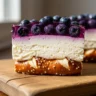 Macro close-up of a slice of Creamy Dream Blueberry Pretzel Delight showing layers of crunchy pretzel crust, creamy white cream cheese, and luscious blueberry topping on a rustic wooden surface.