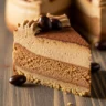 Close-up of a decadent slice of Velvet Espresso Dream Cheesecake with chocolate-covered coffee beans and cocoa powder on a rustic wood board.