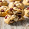Macro close-up of a chewy white chocolate cranberry cookie showing melted chocolate and red cranberries on a rustic wood surface.