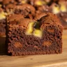 Close-up of a fudgy banana bread brownie slice with a crackled top and melted chocolate chips on a wooden surface.
