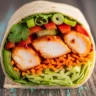 Close-up of a Quick & Zesty Sweet Chili Chicken Power Wrap, cut in half to show succulent chicken, crisp vegetables, and glossy sweet chili glaze wrapped in a tortilla on a rustic wooden surface.