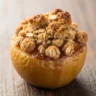 Macro close-up of a single Individual Baked Apple Crisp Bomb with golden streusel topping on a rustic wood surface.