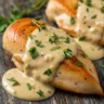 Close-up of golden pan-seared chicken breast smothered in decadent, creamy savory sauce with fresh herbs.