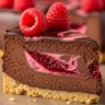 Macro close-up of a slice of Velvet Dark Chocolate Raspberry Dream Cheesecake with a marbled raspberry swirl and fresh raspberries on a rustic surface.