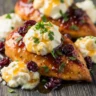 Macro close-up of golden honey cranberry chicken bake with creamy ricotta and fresh parsley garnish on a rustic wooden board.