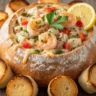 A macro close-up of the Golden Crust Seafood Feast Bread Bowl, overflowing with creamy seafood and melted cheese, garnished with parsley and a lemon wedge.