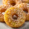 Close-up of golden fried pineapple rings with toasted coconut crust, dusted with powdered sugar.