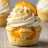 Macro close-up of a Blissful Honey Peach Swirl Cream Cheese Cupcake, garnished with a fresh peach slice and honey drizzle, on a rustic wood surface.