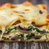Macro close-up of a thick slice of creamy spinach mushroom lasagna with melted cheese, béchamel, and visible vegetable layers.