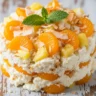 Macro close-up of a vibrant No-Bake Hawaiian Cheesecake Salad with pineapple, mandarin oranges, toasted coconut, and fresh mint garnish.