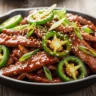 Macro close-up of Sizzling Sweet Heat Jalapeño Beef Stir-Fry with glossy sauce, tender beef, fresh jalapeños, green onions, and sesame seeds.