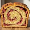 A close-up of a thick slice of Sweet & Tangy Cinnamon Rhubarb Swirl Bread, showing the moist, golden crumb, vibrant pink rhubarb pieces, and a clear cinnamon swirl.