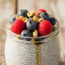 Macro close-up of Velvet Vanilla High Protein Greek Yogurt Chia Pudding in a glass jar, topped with fresh blueberries, raspberries, granola, and maple syrup on a rustic wooden table.