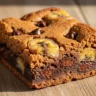Golden Ripe Banana Bliss Blondie with chocolate chips, macro close-up showing fudgy texture on a rustic wooden surface.