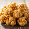 Golden Butterbeer Popcorn Clusters piled high, shimmering with caramel glaze and sea salt flakes on a rustic surface.