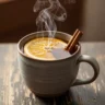 Macro close-up of a steaming Fireside Glow Warm Cinnamon Orange Mocktail in a rustic mug, garnished with an orange slice and cinnamon stick on a dark wood table.
