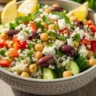 Macro close-up of a vibrant Zesty Mediterranean Lemon-Herb Rice & Chickpea Power Bowl in a rustic bowl, garnished with lemon, fresh herbs, and feta cheese.