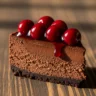 Decadent slice of Velvet Abyss Dark Chocolate Cherry Cheesecake with glistening cherry topping on a rustic wooden board.