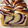 Macro close-up of a freshly baked Cloud-Like Blueberry Cream Cheese Babka, showing golden crust and vibrant blueberry and cream cheese swirls.
