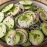 Macro close-up of creamy cucumber ranch salad with red onion and fresh dill in a rustic bowl, showcasing crisp textures.